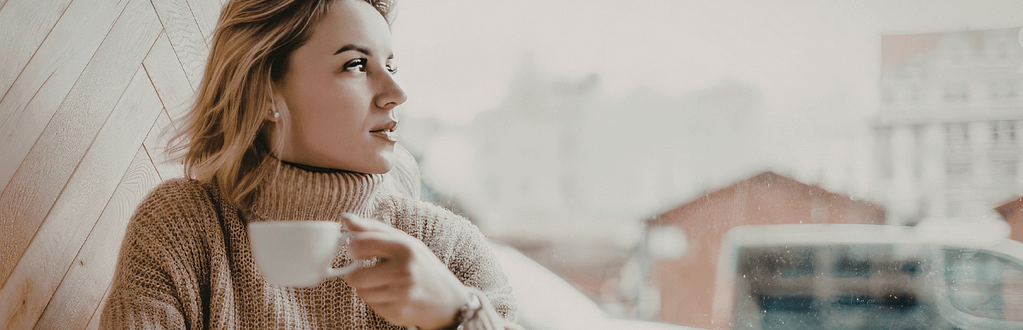 Woman relaxing on a couch with a warm drink and notebook while reflecting on her financial wellbeing and budgeting goals.