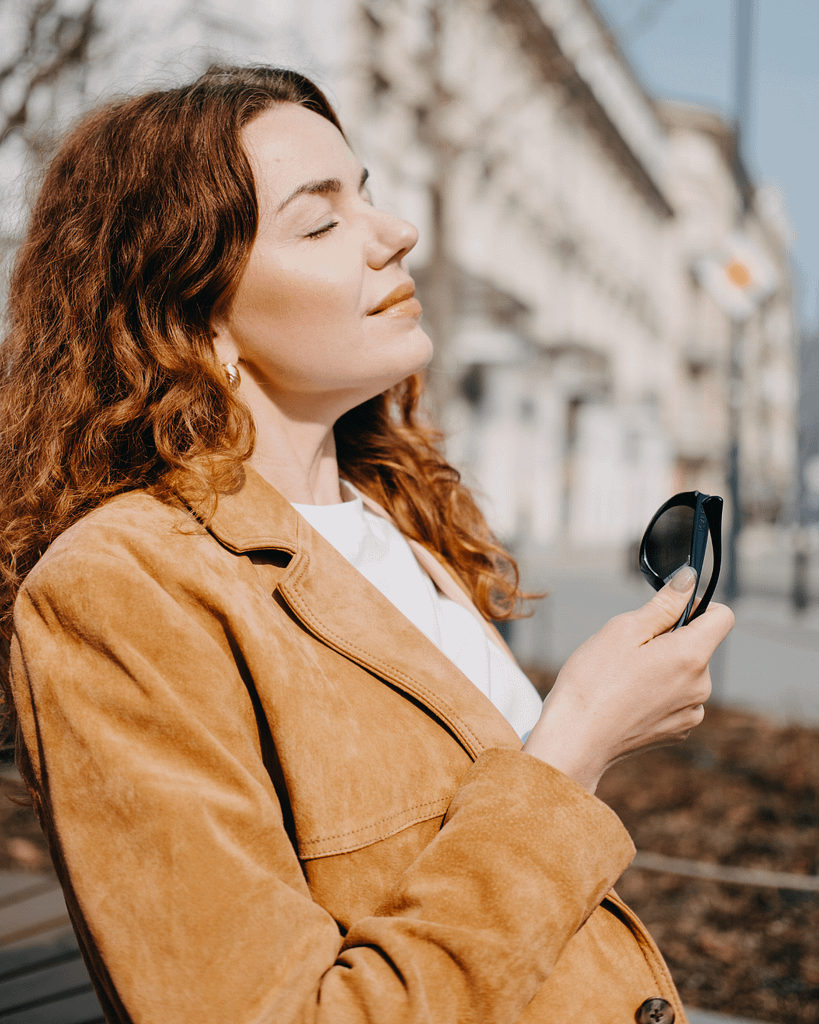 Woman standing outdoors peacefully with eyes closed during a calm emotional and financial wellbeing reset moment.